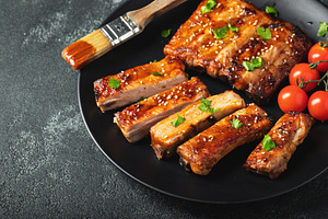Hot grilled spare ribs from a summer BBQ served on a plate with sauce. Top view, a Food & Drink Photo by Budarinphoto