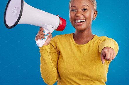Black woman, megaphone and pointing, protest and voice, freedom of speech and activism on blue background. Happy female, broadcast and speak out, rally and portrait, loudspeaker and opinion in studio, a Photo by Peopleimages.com