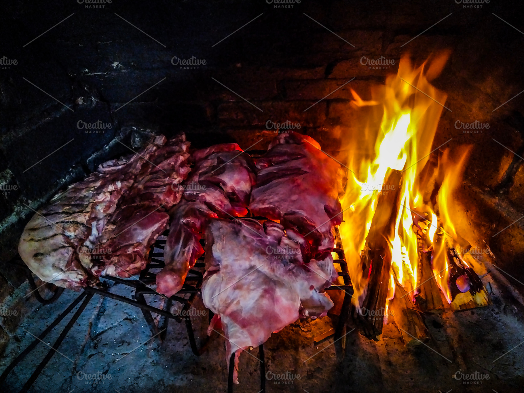 Raw meat sizzling on the grill beside an open fire, a Food & Drink Photo by DanFLCreativo