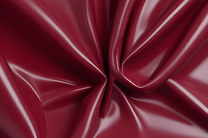 A close-up of deep red glossy leather fabric with soft, flowing folds illuminat