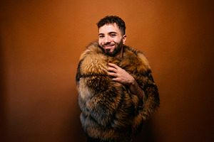 Confident man wearing luxurious faux fur coat smiling, a Photo by karrastock