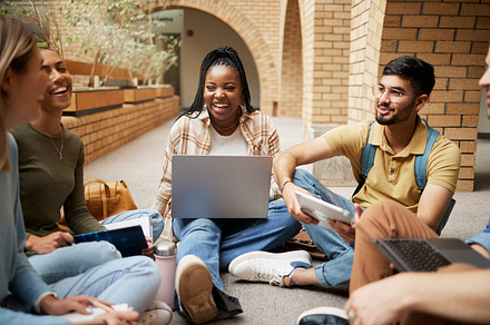 Diversity, laptop and students on ground, conversation and connection for study session, brainstorming and group project. Academics, young people or friends sitting, talking and collaboration outdoor, a Photo by Peopleimages.com