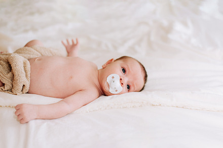 newborn with a pacifier in studio lighting against white, a Person Photo by rubenchase