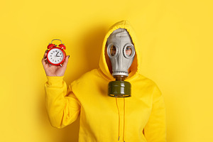 Individual wearing yellow hoodie and gas mask holds red alarm cl, a Person Photo by Ales Munt