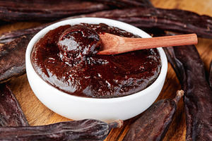 thick carob spread surrounded by dried carob pods, a Photo by Nito