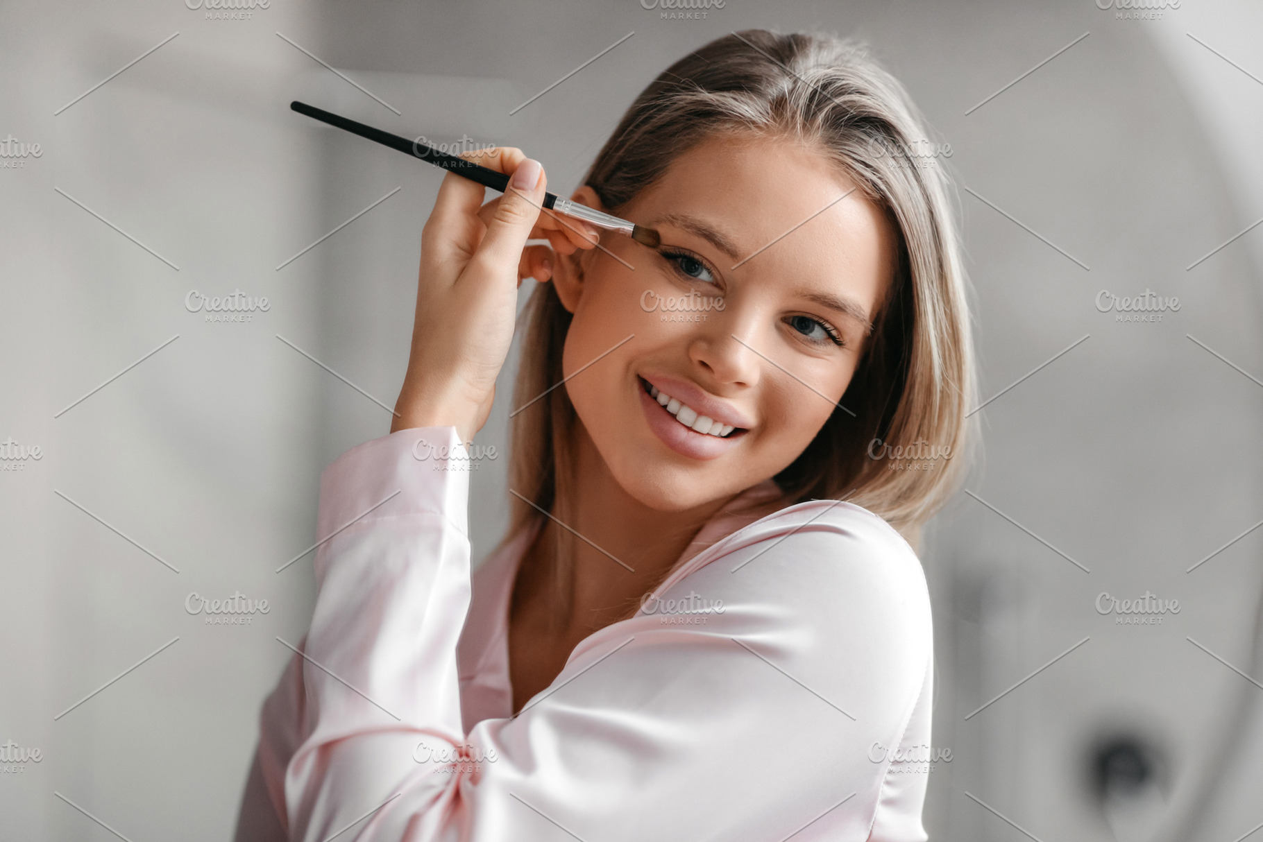 Sensual lady applying eye shadow with applicator near mirror in bathroom interi, a Photo by Prostock-Studio