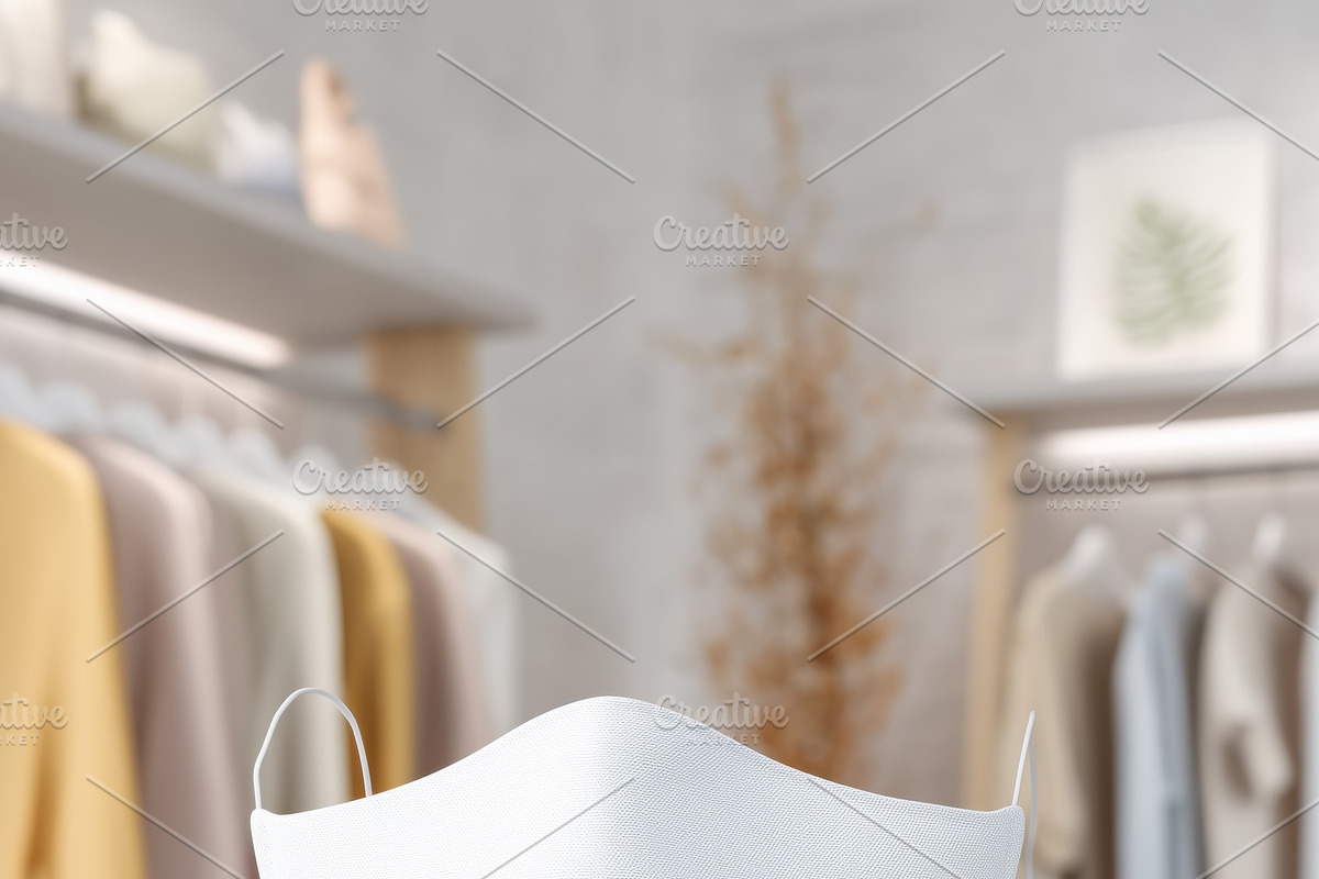 A white face mask mockup on a stand in a modern clothing store, with soft paste, a Mask Mockup by Textures & Backgrounds