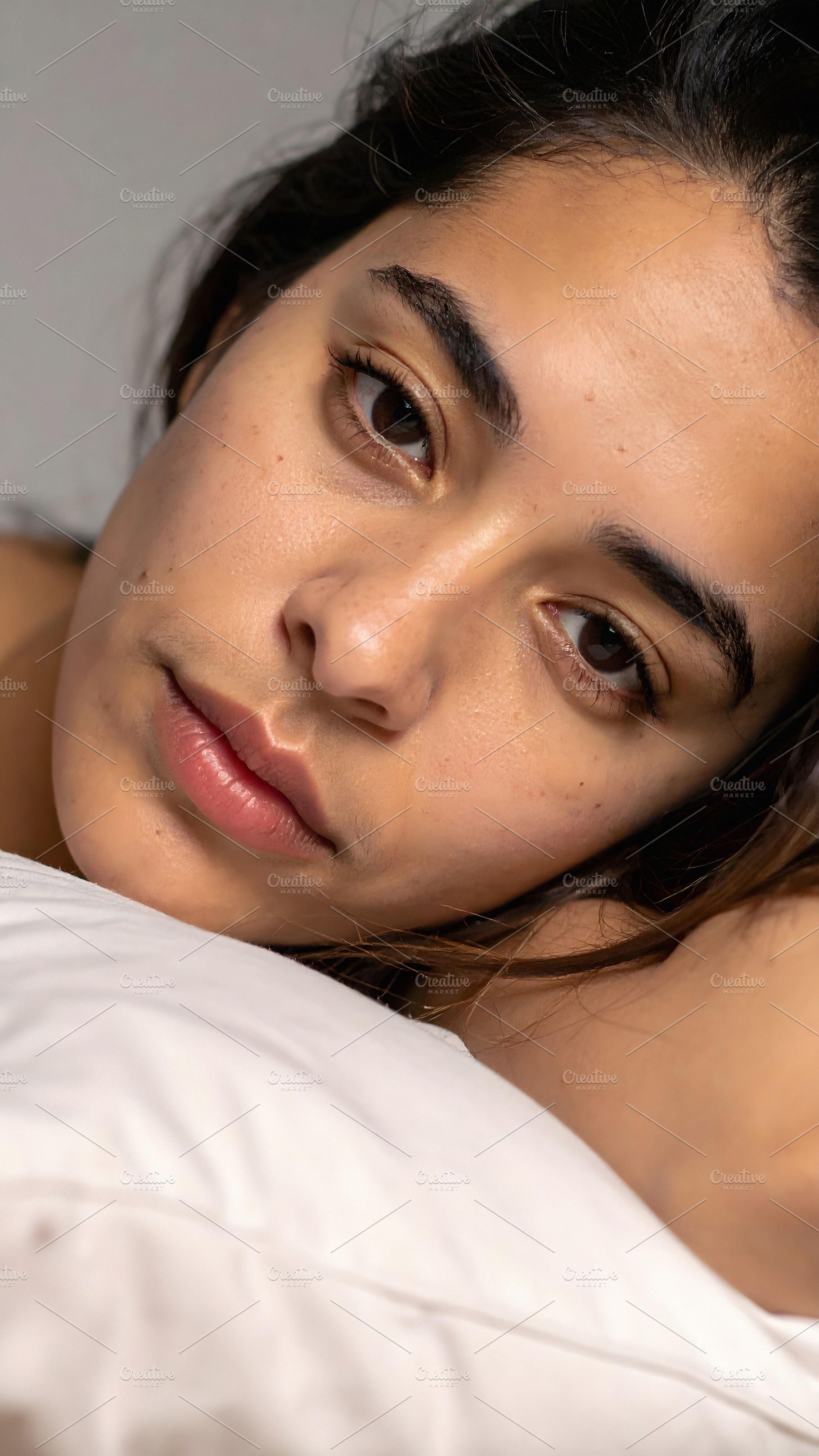 Young woman lying on pillow with soft relaxed gaze, a Person Photo by GoodGoods