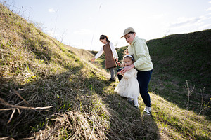 Older brother helping little sister walk up grassy hill during family outing in, a Person Photo by AS photostudio