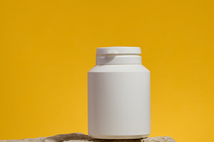 White plastic medicine jar on stone, yellow background. Mock up, a Health & Medical Photo by ndanko