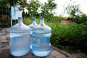Three large water containers placed outdoors in a lush green garden area, a Photo by AS photostudio