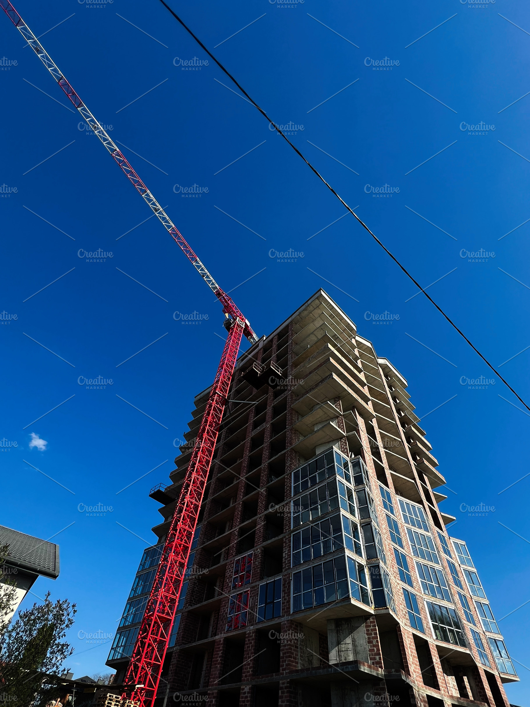 Red construction crane working at tall building under a clear blue sky, a Photo by AS photostudio
