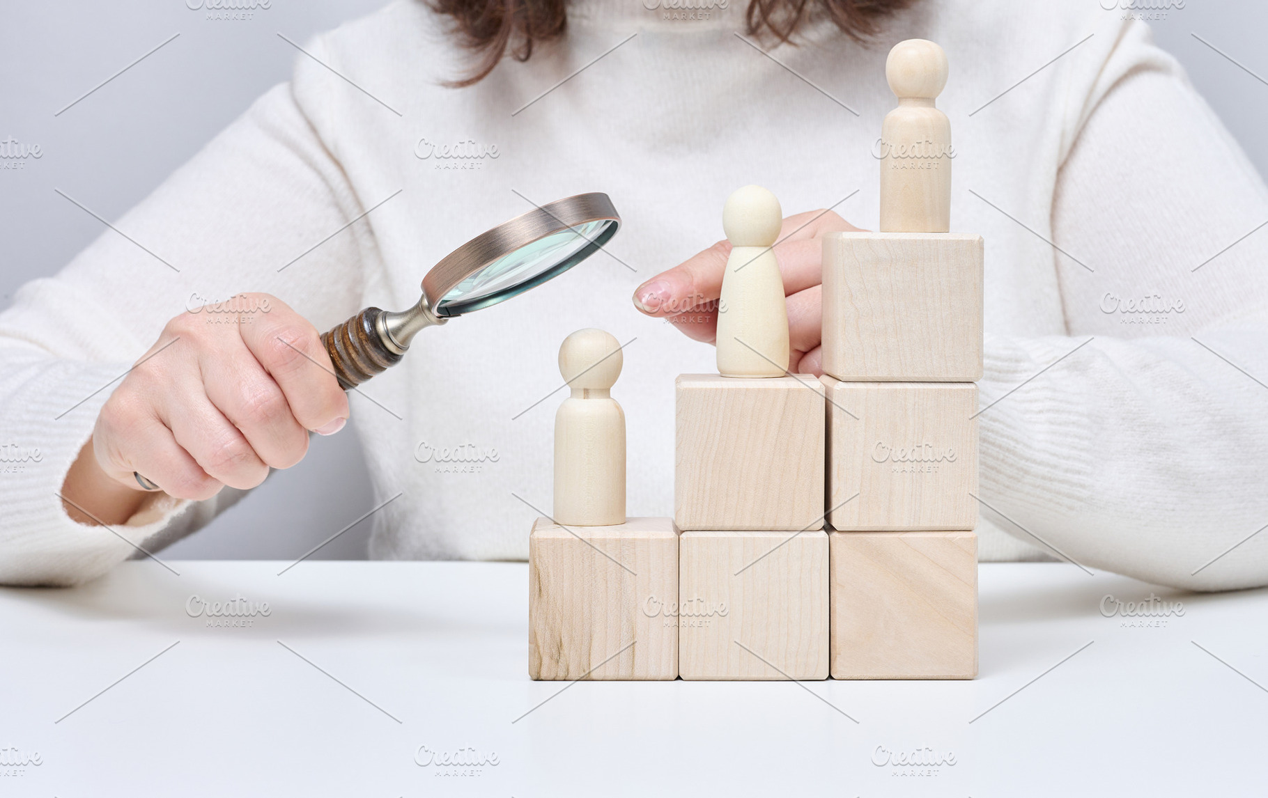 A man with a magnifying glass examines wooden figures on cubes i, a Person Photo by ndanko