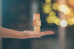 Hand, building blocks and balance with a business woman holding wood for growth on a blurred background. Investment, portfolio and stack with the foundation of a company built on financial stability, a Photo by Peopleimages.com