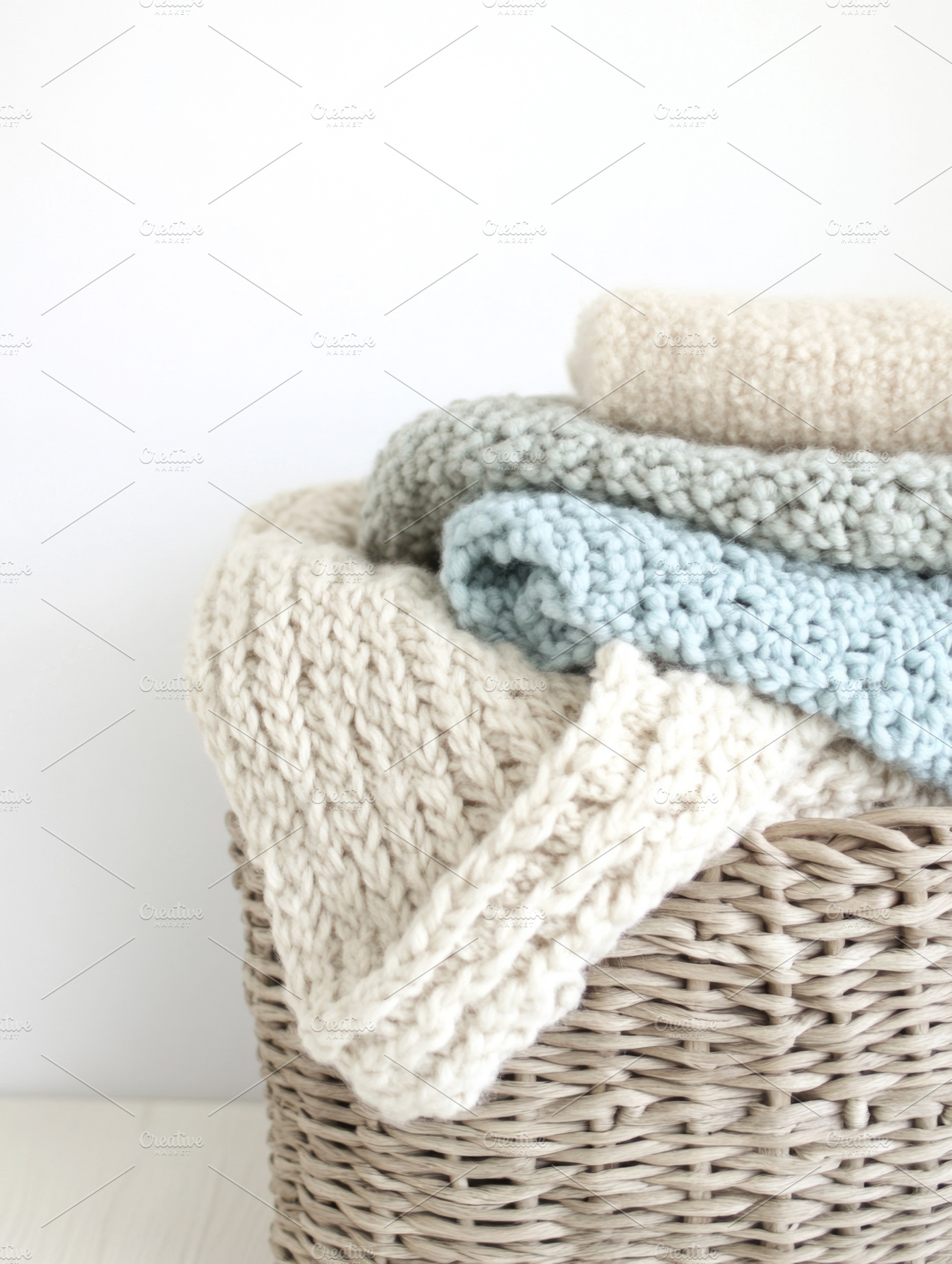 Pastel-colored knitted blankets stacked in basket on white backg, a Photo by Dvoevnore photos