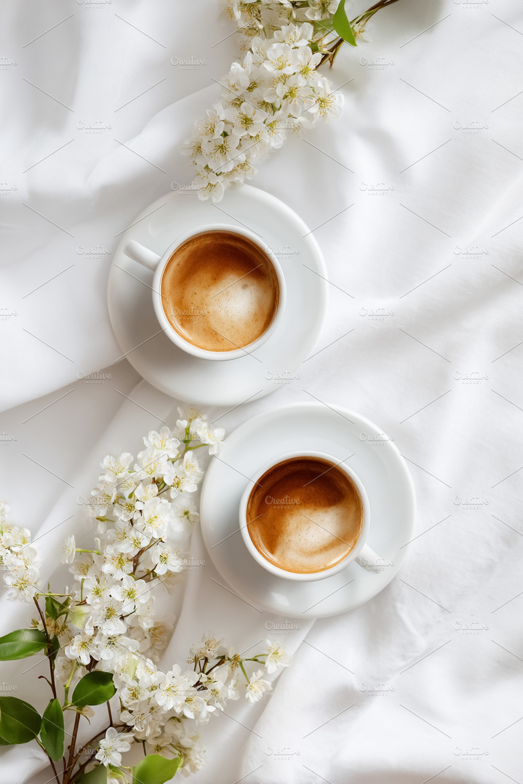 Two cups of coffee with spring white flowers on pristine fabric,, a Photo by Studio ANNA