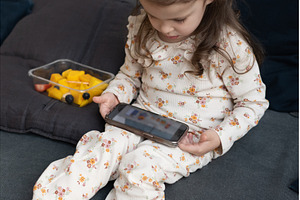 Toddler girl sits on home sofa, a Technology Photo by undrey