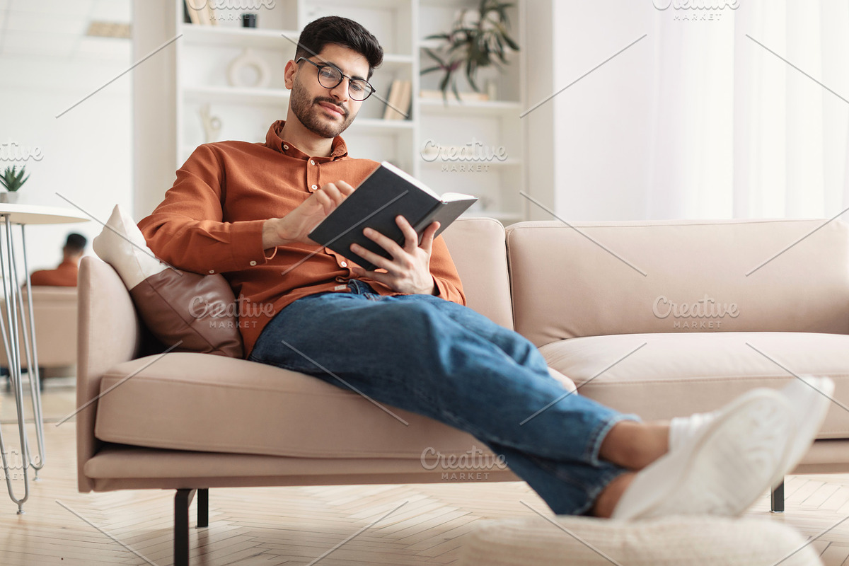 Smiling Arab man in glasses reading paper book, a Photo by Prostock-Studio (Photo 1 of 2)