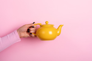Hand holding a bright yellow teapot against a pastel pink backgr, a Food & Drink Photo by Ales Munt