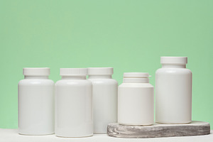 Several white plastic jars with pills on a green background. Ite, a Health & Medical Photo by ndanko