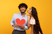 St. Valentine's day. Pretty indian woman kissing smiling man, holding red heart, a Photo by Prostock-Studio (Thumbnail 2 of 3)