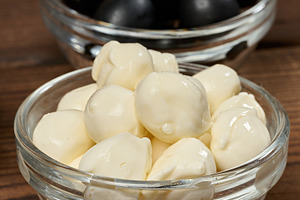 Mozzarella balls in a glass bowl in the foreground, blurred oliv, a Food & Drink Photo by ndanko