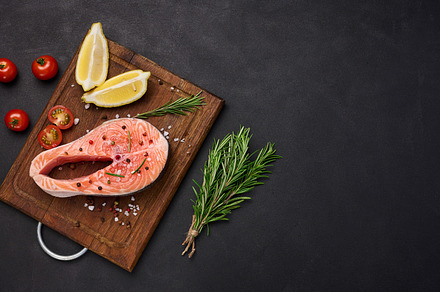 Raw salmon steak on a wooden cutting board, lemon slices, spices, a Food & Drink Photo by ndanko