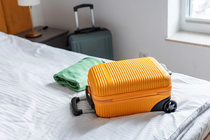Orange suitcase and folded clothes resting on hotel bed, a Holiday Photo by Olena Rudo