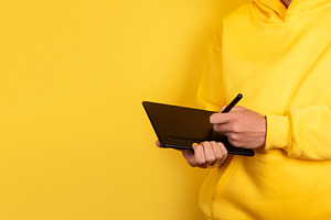Person in yellow hoodie using digital pen tablet against vibrant, a Technology Photo by Ales Munt