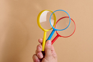 A person is holding three multicolored plastic magnifying glasse