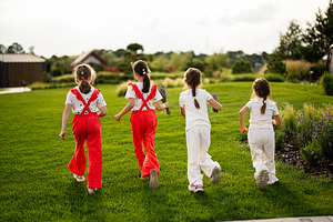 Children running on lush green grass in a peaceful countryside setting, a Photo by AS photostudio