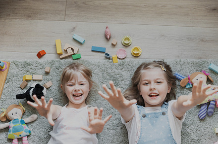 Two small sisters playing with different toys at home, lying on the floor, a Photo by Lenor4ik