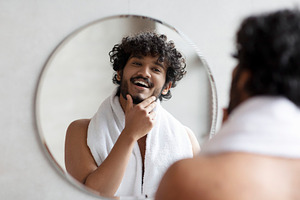 Male facial skincare concept. Young indian man touching beard, caring for skin, a Person Photo by Prostock-Studio