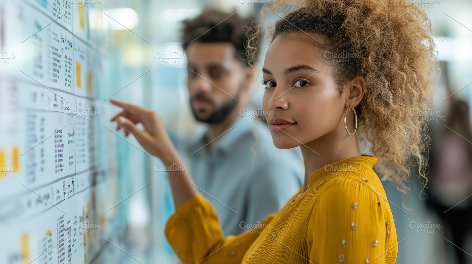 Young Black woman in a yellow blouse examines information on a board, while a m, a Person Photo by ImageMir