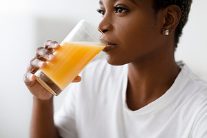 Cropped thirsty young pretty black lady in white t-shirt drinks fresh orange ju, a Person Photo by Prostock-Studio