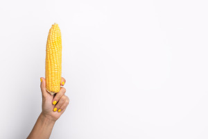 Female hand with yellow nail polish holding an ear of corn agai, a Food & Drink Photo by Ales Munt