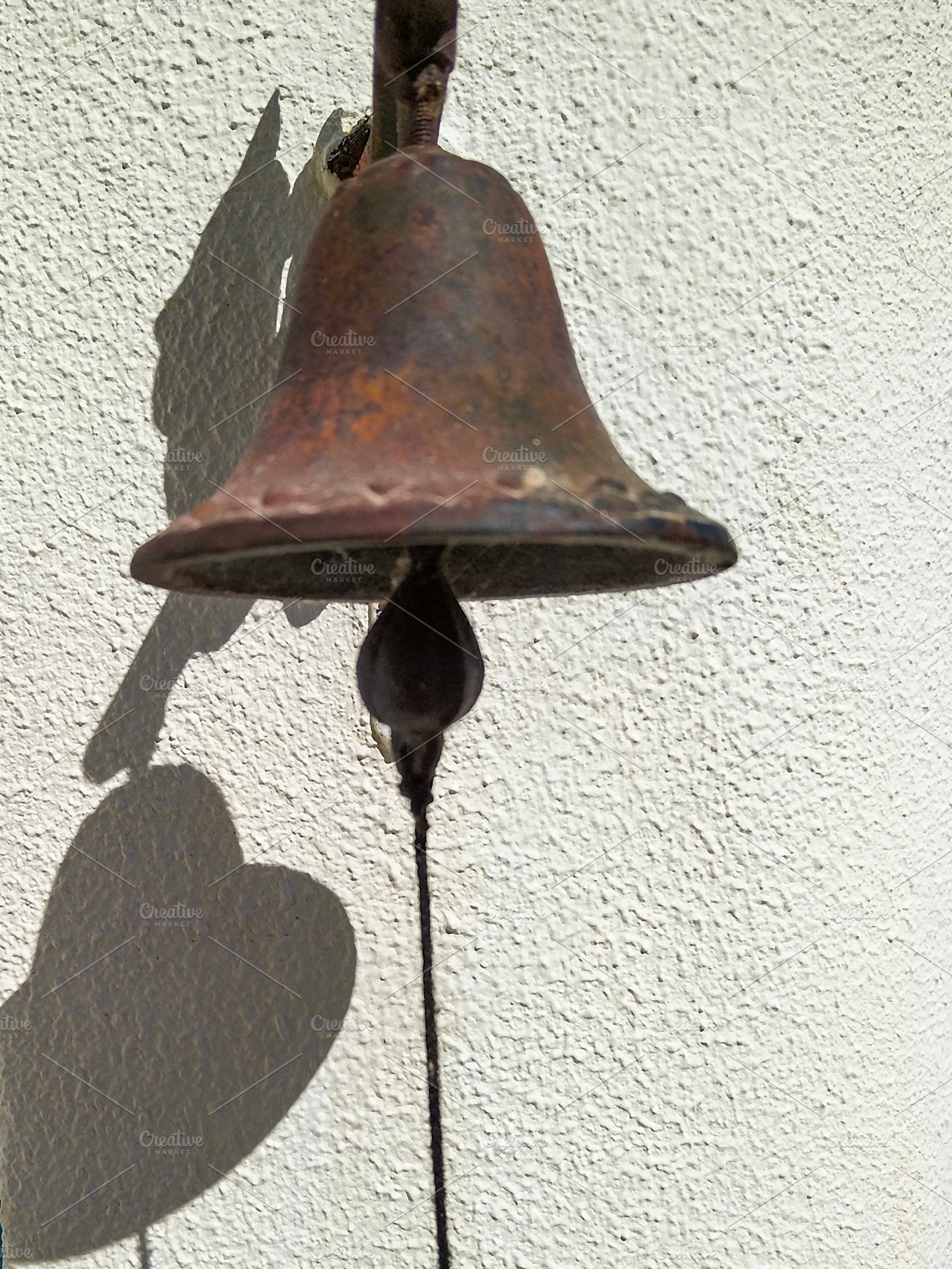 Close-up of a rustic bell casting a shadow on a white wall, an Arts & Entertainment Photo by DanFLCreativo