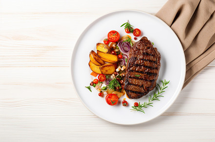 Grilled meat steak with vegetables in plate on white wooden background, a Food & Drink Photo by AlyaAnd