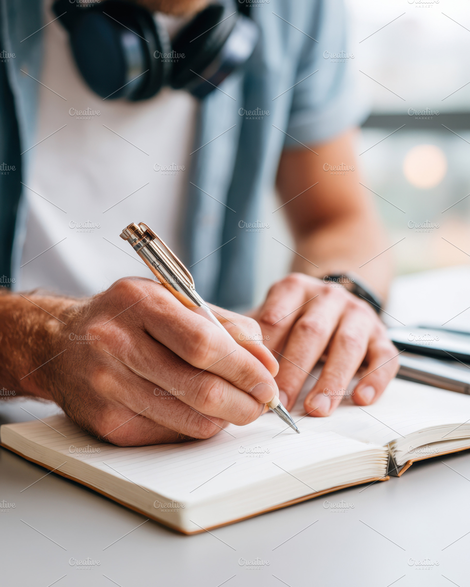 Person writing in notebook with headphones, a Business Photo by AlyaAnd