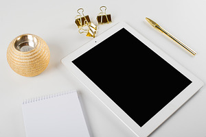 Tablet and notebook next to ballpoint pen and golden clips on white background.