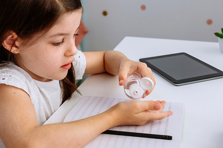 Girl applying hand sanitizer while doing homework, a Person Photo by davidpereiras
