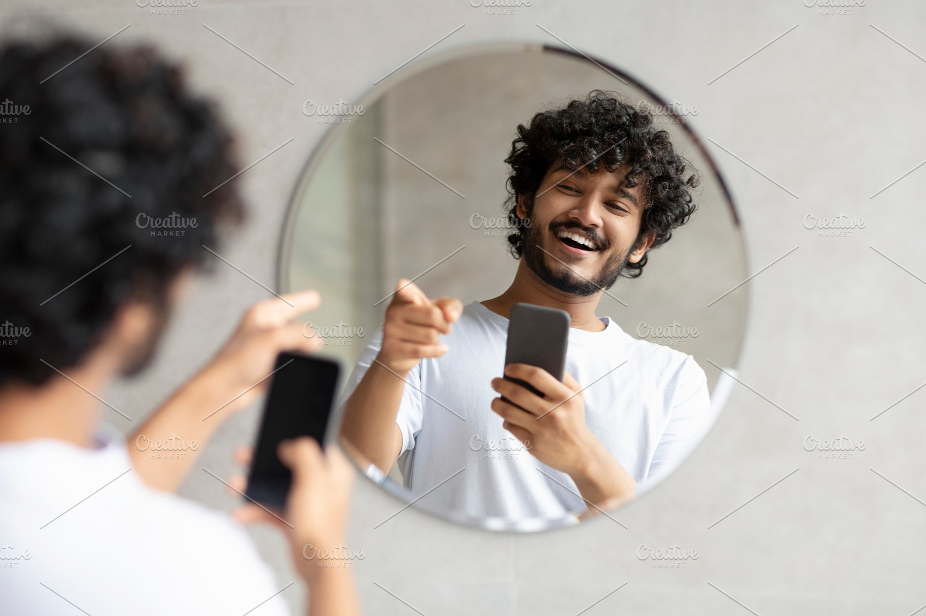 Excited indian guy taking photo in bathroom mirror holding smartphone and point, a Person Photo by Prostock-Studio