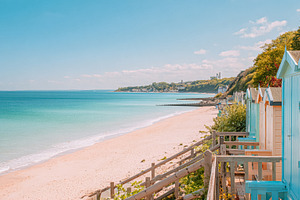 Beach huts lining a sandy shore with turquoise ocean under a cle, a Photo by Studio ANNA