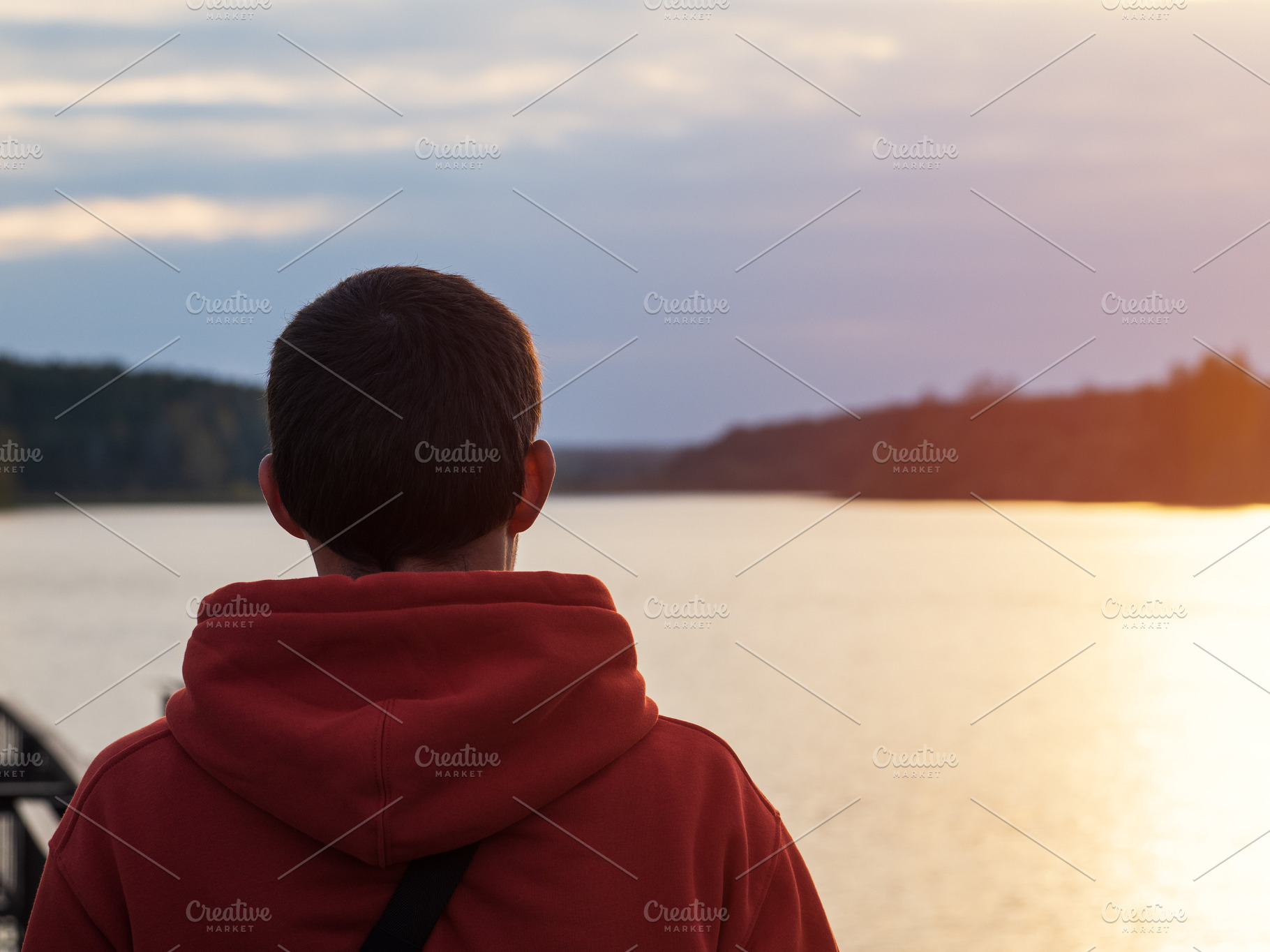 A man in an orange hoodie looks at a cloudy autumn sunset by the lake. Lifestyl, a Person Photo by PavelKant