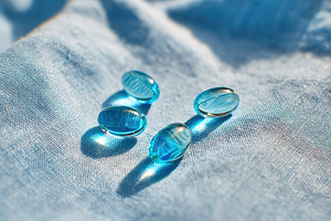 Glossy blue capsules resting on a soft fabric under bright lighting conditions, a Photo by AlyaAnd