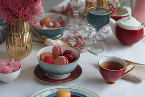 Elegant afternoon tea service setting with colorful macarons, hot tea, flowers, a Food & Drink Photo by Studio ANNA