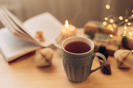 Cozy winter still life. Mug with tea or coffee, burning candle, book, gift box