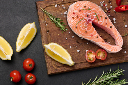 Raw salmon steak on a wooden cutting board, lemon slices, spices, a Food & Drink Photo by ndanko