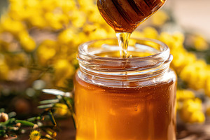 Close-up of a small glass jar filled with golden honey and a honey dipper again, a Photo by AlyaAnd