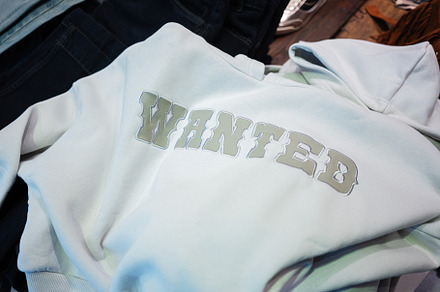 White hoodie with Wanted printed text displayed on a wooden background, a Photo by AS photostudio